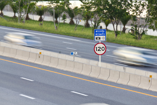 Speed limit (120 km/hour) and speed camera signpost on motor way with cars in motion