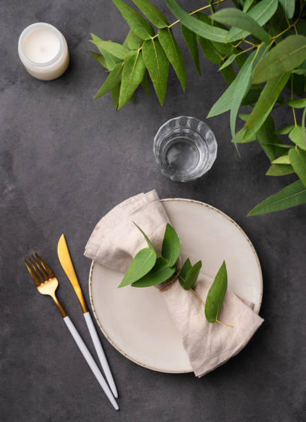 istock Celebration table setting with a beige plate, a glass, a candle and a napkin with eucalyptus branches on a dark background. Rustic style. 1735075912