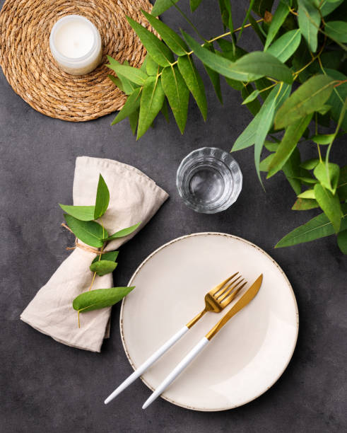 istock Table setting with a beige plate, a glass, a candle and a napkin with eucalyptus branches on a dark background. Rustic style. 1735076446