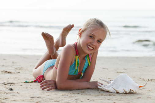 Young girl lying on the beach with seashell.