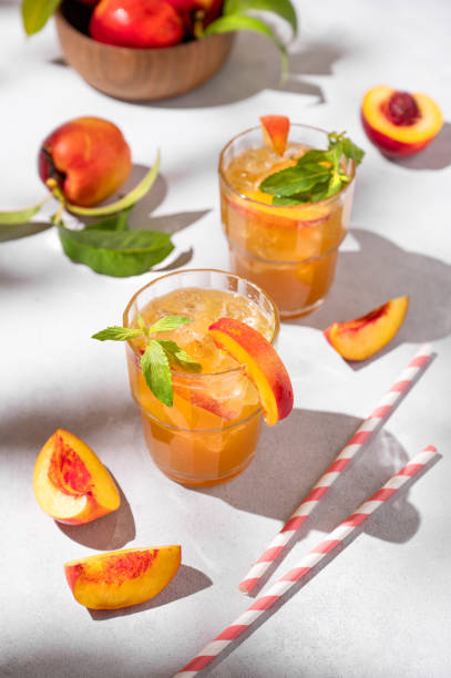 deux verres avec du thé à la pêche rafraîchissant avec de la glace et de la menthe. boisson d’été froide faite maison sur un fond clair avec des fruits frais et des ombres. - georgia peach photos et images de collection