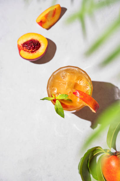 освежающий перси�ковый чай со льдом и мятой. домашний холодный полезный напиток на светлом фоне со свежими фруктами, пальмовым листом и теня - georgia peach стоковые фото и изображения