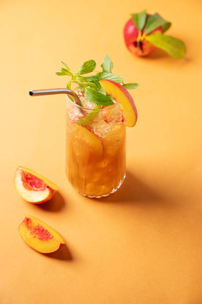 освежающий персиковый чай со льдом и мятой. веганский домашний холодный летний напиток на оранжевом фоне со свежими фруктами. - georgia peach стоковые фото и изображения