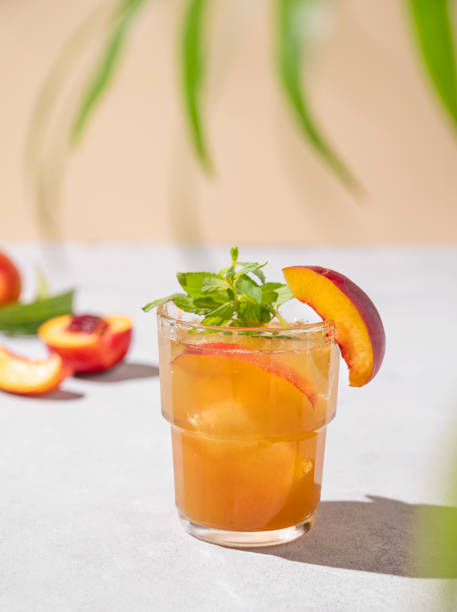 персиковый чай со льдом и мятой. домашний холодный полезный вегетарианский напиток на светлом фоне со свежими фруктами, пальмовым листом и  - georgia peach стоковые фото и изображения