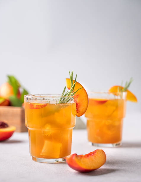 deux verres de thé à la pêche avec de la glace et du romarin. boisson froide végétarienne et saine faite maison sur un fond léger avec des fruits frais. - georgia peach photos et images de collection