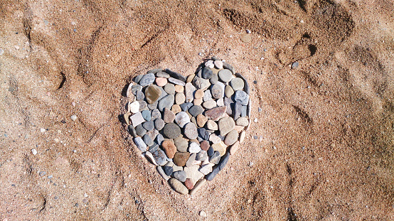 Sea pebbles in the shape of a heart on a sandy beach. Romantic holiday concept or symbol of love. Top view and copy space.