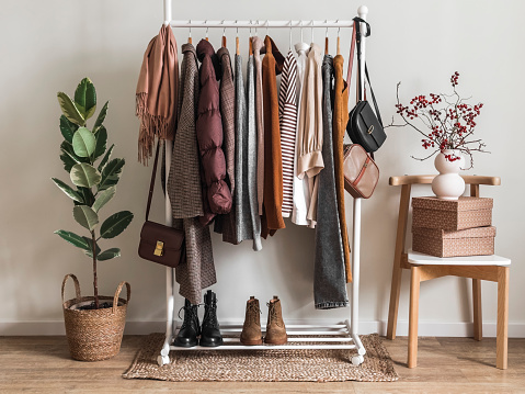 Cozy dressing room. Floor hanger with women's seasonal autumn winter clothes. Coats, pullovers, jackets, shirts, shoes - comfortable casual women's clothing