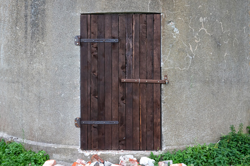 A brown wooden door on the concrete wall of a round gray tower is closed with an iron bolt. Background. Architecture.