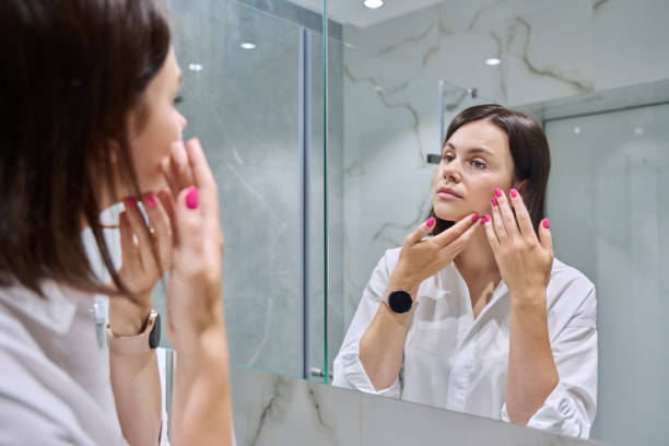 istock Young woman looking at her face in bathroom mirror 1735108823