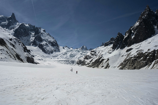 Before Mont Blanc (Monte Bianco) summit 4808m last ascending. Team roping up Man with climbing axe dressed high altitude mountaineering clothes with backpack walking by snowy slopes with blue sky.