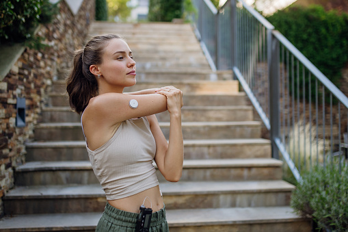 Beautiful diabetic woman preparing for outdoor run in the city. Young woman wearing an insulin pump during exercising. Concept of exercise and diabetes.