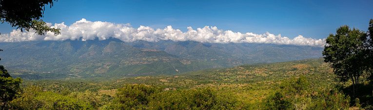 Panoramic aerial view from the plateau to the valley and adjacent mountains covered with white clouds, blue sky, Barichara, Colombia
