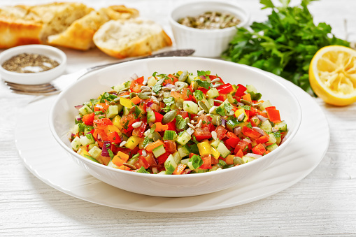 Israeli salad of finely diced tomato, onion, cucumber, and bell peppers, salat katzutz, salat aravi, salat yerakot in white bowl on white wooden table, horizontal view