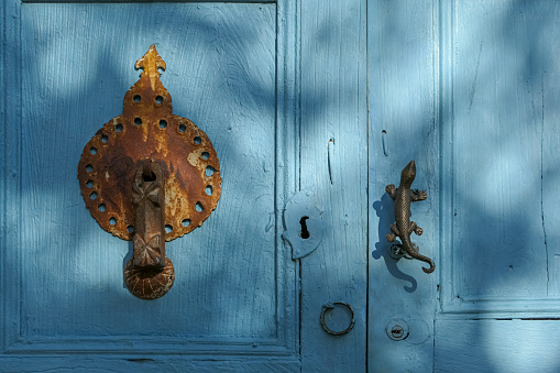 Historic door knocker and handle on a turquoise door in light and shadow, Barichara, Colombia