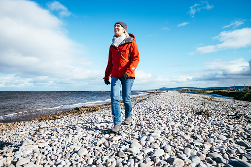 Woman enjoying a stroll along the pebble beach at Kingston, Spey Bay, Moray, Scotland.