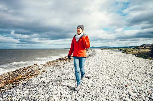 Woman enjoying a stroll along the pebble beach at Kingston, Spey Bay, Moray, Scotland.