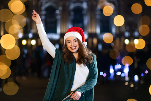 Smiling girl with bright makeup outdoors at night with sparklers. Young woman celebrating the event is approaching New Year
