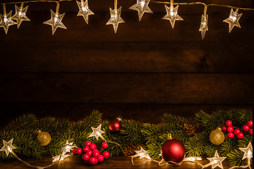 Front view of a group of christmas ornaments arranged at the bottom of the image and some christmas lights at the top leaving a useful copy space at the center of the image on a rustic wooden table