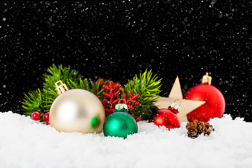 Front view of a group of christmas ornaments such as pine twigs, christmas balls, wooden star shapes and berries standing on the snow with copy space on black background
