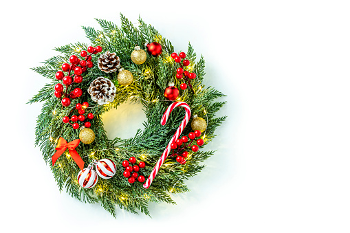 Top view of a christmas wreath with ornaments such as a candy cane, christmas balls, berries and christmas lights isolated on white background