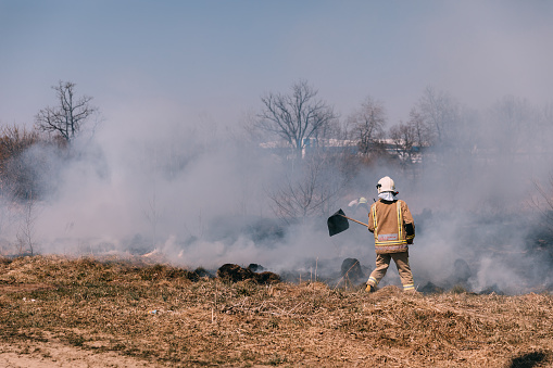An adult of unknown sex and age, shrouded in protective gear, feeds the flames of a controlled burn in the wetlands of the Blackwater Wildlife Refuge near Cambridge, MD