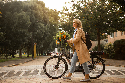 Beautiful blonde middle aged woman cycling with sunflowers in a local dutch neighbourhood during the day in Autumn