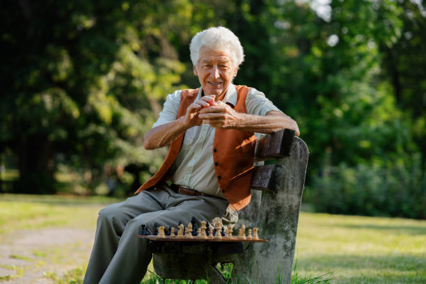 portret starszego mężczyzny na wózku inwalidzkim z szachami na ławce znajduje się samotnie w miejskim parku, czując się samotny. - arthritis senior adult rheumatoid arthritis sadness zdjęcia i obrazy z banku zdjęć