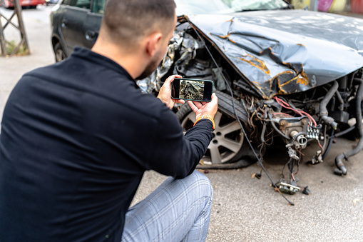 A young man assesses and documents the car damage efficiently using his mobile device