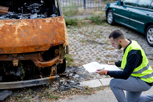 A young man thoroughly evaluates the damage on the combination vehicle, meticulously recording his findings in a notebook