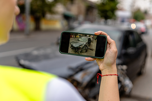 The young woman, using her mobile phone, captures detailed images of her car's damage after the collision
