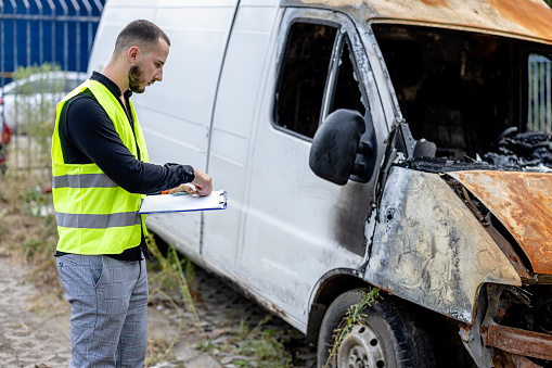The young man assesses the van's damage and promptly writes a detailed report in his notebook
