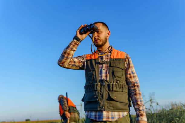istock Young and curious son looking through binoculars, while his mature hunter father is walking in the field and holding a rifle 1735232964