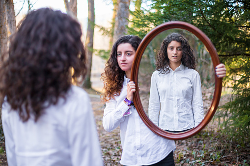 Young woman showing reflection of twin sister in autumn day in the forest