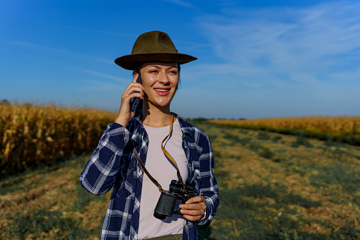 Young Caucasian cheerfully woman talking on a mobile phone, while holding binoculars in her hand and smiling.