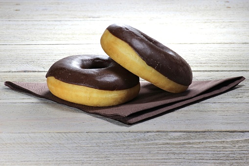 chocolate iced donuts with napkin on wooden background