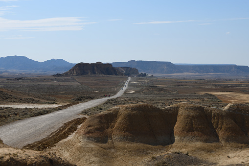 The photo shows the badlands of Bardenas Reales National Park. There is a road running from the left foreground into the distance. The erosion is clearly shown. In the distance is a big plateau and in front of it a mesa. The sky is blue.

The photo is taken in the Bardenas Reales (sometimes referred as Bárdenas Reales) national park. It is a semi-desert natural region, or badlands, of some 42,000 hectares (420 km2; 104,000 acres) in southeast Navarre, bordering Aragon, Spain. It is located in the middle of the depression of the Ebro valley, at the foot of the mountains of the Yugo and the Zaragoza region of Cinco Villas, and is a UNESCO Biosphere Reserve.  It comprises of the natural Reserve ‘Rincón del Bú’ and the Reserva Natural ‘Caídas de la Negra’ .The photo was taken in May2023