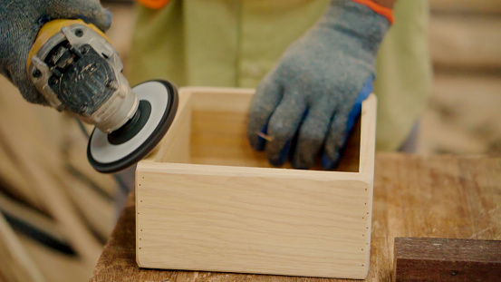 Close up hand asain senior carpenter using sander \n box wood in home workshop.
