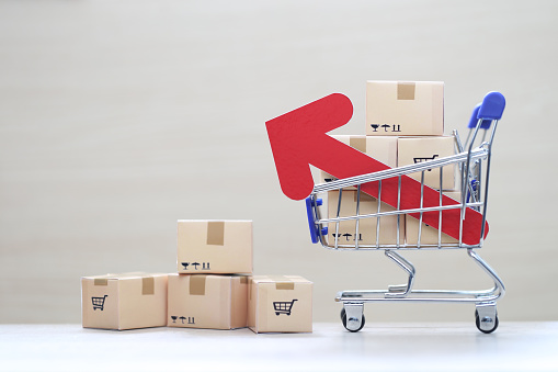 Global inflation or Deflation concept, Red arrow graph and brown parcel box on model miniature shopping cart on wooder background,Hyperinflation