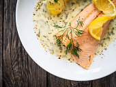 Roasted salmon fillet and cooked potatoes in creamy dill sauce on wooden background