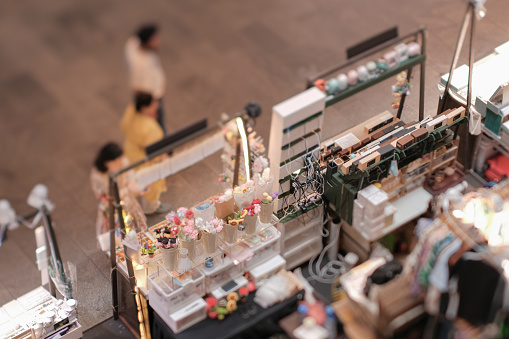 High angle view of customers at indoor festive weekend market. Social pop up event in shopping mall for entrepreneurs and makers. Captured with a tilt-shift lens. Selective focus; bokeh effect.