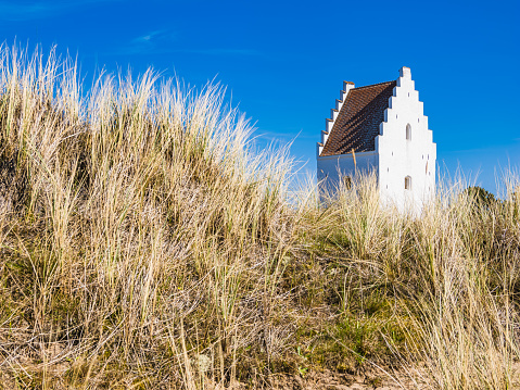 Old church in Skagen among land and prairies with blue sky.