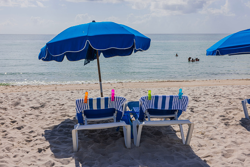 Beautiful view of Atlantic Ocean on sandy Miami Beach with blue sun loungers and umbrellas. USA.