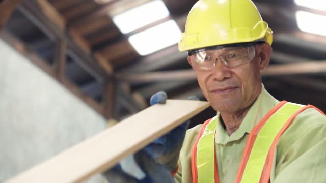 Asian senior carpenter checking the edge of a timber, to see if he cut it on the right angle.