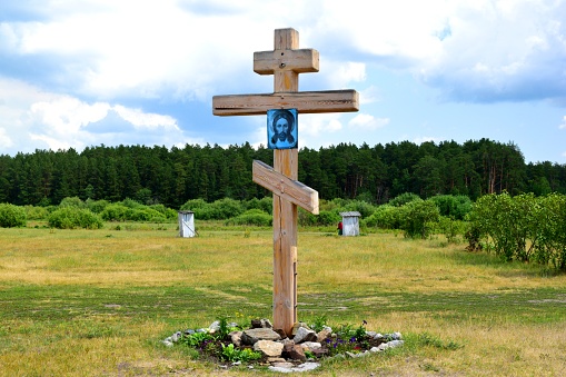 An Orthodox cross with an icon of the Lord Jesus Christ on the background of a forest and a blue sky.