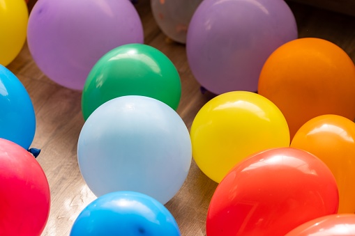 A portrait of multiple vibrant balloons lying on a living room floor indoor of a house. The fun decorations are ready for a home birthday party or anniversary celebration. Kids can play with them.