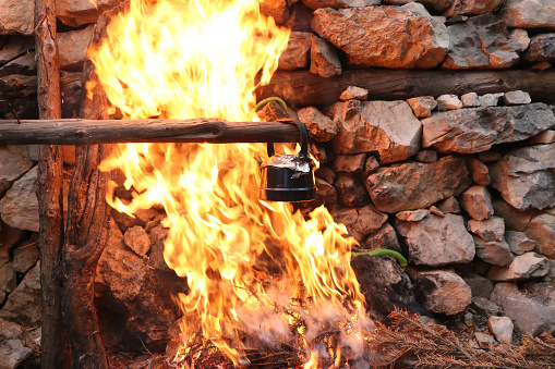 A grey kettle cooking on a campfire with flames surrounding it.
