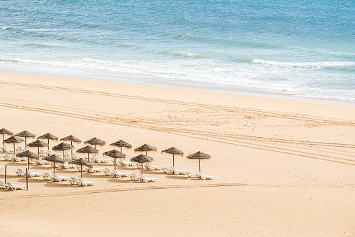 Empty beach with parasol and sun lounger by the ocean.