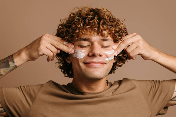 istock Handsome man enjoying beauty treatment while applying cream on face and standing on brown background 1735407621