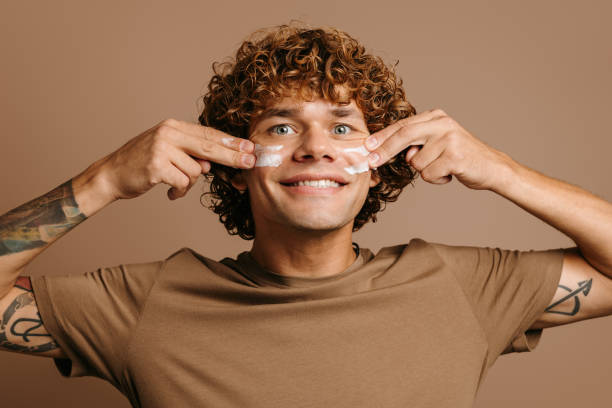 istock Handsome man enjoying beauty treatment while applying cream on face and standing on brown background 1735407627