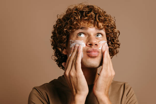 istock Handsome man enjoying beauty treatment while applying cream on face and standing on brown background 1735407647
